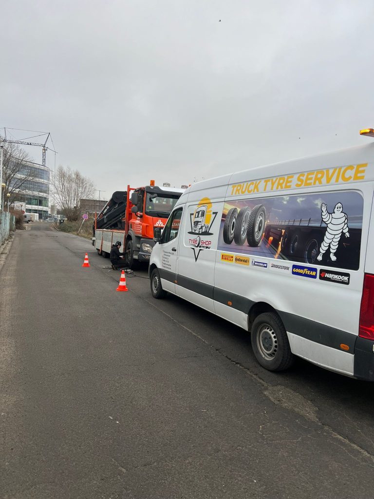 La camionnette Truck Tyre Service garée derrière un camion en panne, cônes de signalisation posés sur la chaussée