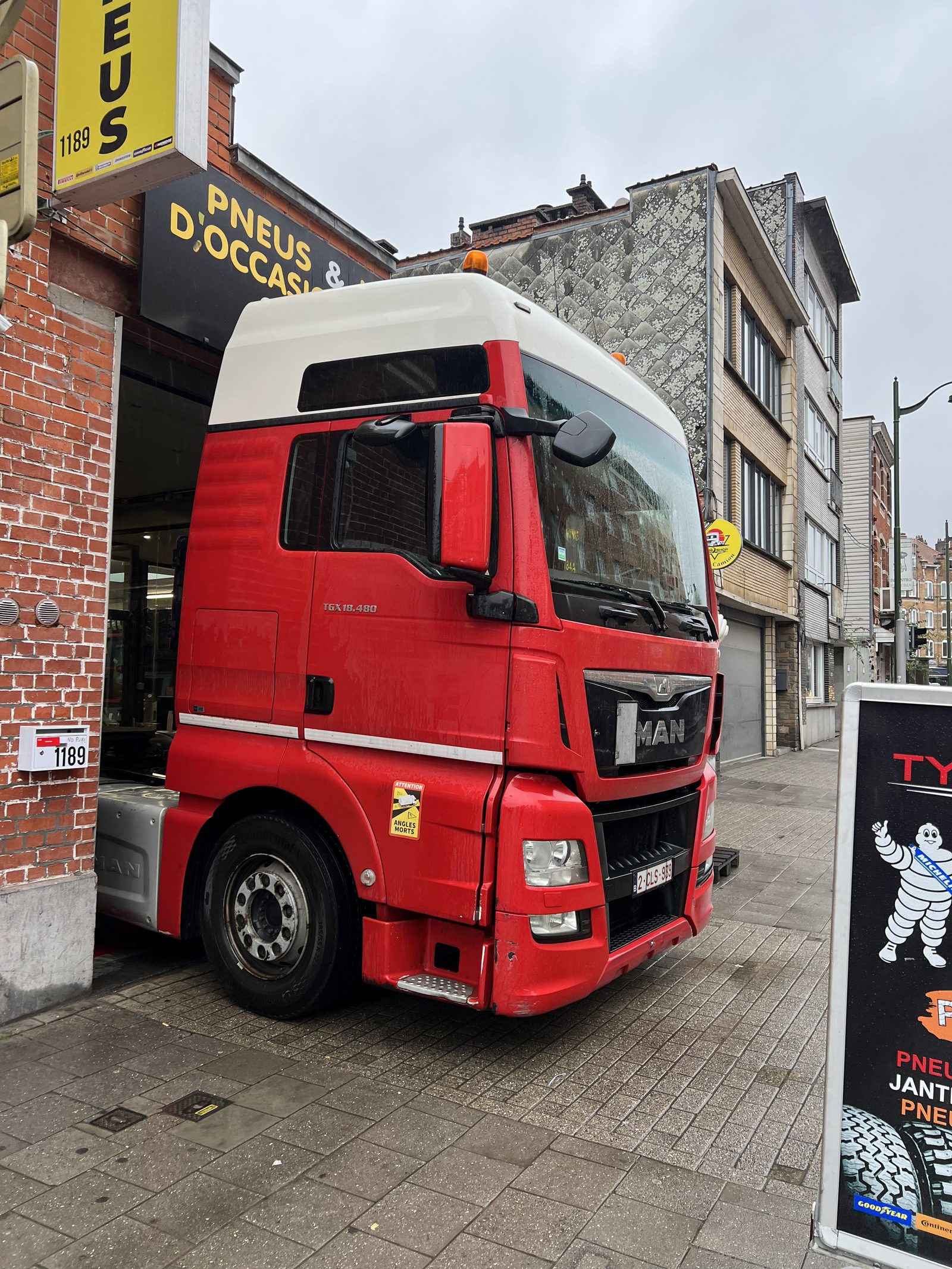 Un tracteur routier MAN rouge stationné devant l'atelier, chaussée de Mons